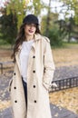 A beautiful smiling girl wearing a light coat, jeans and a baseball cap is walking in the autumn through the park along the fallen