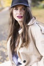 A beautiful smiling girl wearing a light coat, jeans and a baseball cap is walking in the autumn through the park along the fallen