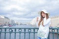 A beautiful and smiling girl in a white hat with wide brim is standing on the bridge and talking on the phone against the backgrou Royalty Free Stock Photo