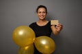 Beautiful smiling happy woman dressed in black outfit shows inflated air balloons of gold color and gold empty blank credit card. Royalty Free Stock Photo