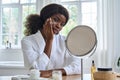 Young happy black girl applying facial cream in front of mirror in bathroom. Royalty Free Stock Photo