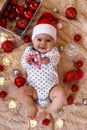 Beautiful smiling little girl in Santa Claus red hat is playing with wooden toy on a beige plaid with Christmas decorations. Royalty Free Stock Photo