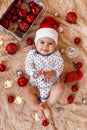 Beautiful smiling little girl in Santa Claus red hat is playing with wooden toy on a beige plaid with Christmas decorations. Royalty Free Stock Photo