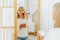 Beautiful smiling mature senior caucasian woman with blonde hair standing near mirror with make up palette and brush Royalty Free Stock Photo