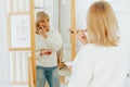 Beautiful smiling mature senior caucasian woman with blonde hair standing near mirror with make up palette and brush Royalty Free Stock Photo