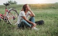 Beautiful smiling mature woman sitting next to bike on the grass on a green field. Summer Country Vacation Adventure Concept Royalty Free Stock Photo