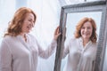 beautiful smiling mature woman standing near mirror and looking