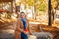 Beautiful smiling middle aged blonde woman wearing beige coat and scarf, sitting in city park on sunny autumn day Royalty Free Stock Photo