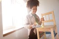 A beautiful smiling mixed-race girl wipes a wooden chair with a rag. An attractive young African woman is preparing furniture for Royalty Free Stock Photo