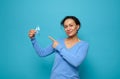 Beautiful smiling mixed race woman in blue shirt points to blue satin diabetes awareness ribbon in hand, posing against colored