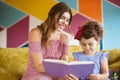 Beautiful smiling mother with her little pretty daughter happily drawing in book with felt-tip pens while spending time