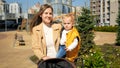 Beautiful smiling mother holding her baby son and walking with stroller on the playground. Happy parenting, family having time Royalty Free Stock Photo