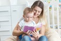 Beautiful smiling mother reading book to her 9 months old baby b Royalty Free Stock Photo