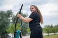 Beautiful smiling overweight young woman does fitness on an ellipsoid simulator outdoors. Fat girl is training on the