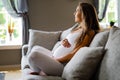 Smiling pregnant woman sitting in sofa touching her belly Royalty Free Stock Photo