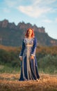 Beautiful smiling red-haired lady with a traditional blue dress decorated with goldwork in a field