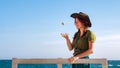 A beautiful smiling red-haired traveler girl throws a pebble in her hand against the background of the sky and the sea. Royalty Free Stock Photo