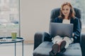 Smiling red-haired woman working in headphones on laptop computer in modern open plan office Royalty Free Stock Photo