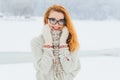 Beautiful smiling red head woman with glasses is wrapped in the scarf during the snowfall in the forest. Half-length Royalty Free Stock Photo