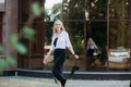 woman with long blond hair, in a black long dress and a white shirt, walks along the city street Royalty Free Stock Photo