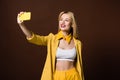 beautiful smiling stylish blonde girl taking selfie with yellow smartphone