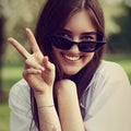 Beautiful smiling teen woman looking happy in fashion black sun glasses, making funny mug and showing the tongue on green glass Royalty Free Stock Photo