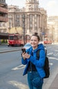 Beautiful smiling tourist woman with mobile phone and backpack standing near road in the Belgrade city, Serbia Royalty Free Stock Photo