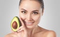 Beautiful smiling woman with clean skin holds ripe avocado near the face. Cosmetology skin care