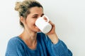 Beautiful smiling woman drinking cappuccino. Happy young woman drinking hot beverage at home. Charming blonde female holding a Royalty Free Stock Photo