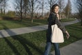 Beautiful smiling woman with an eco white bag on her shoulder walks in the park and looks at the camera. Millennials go