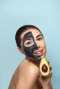 Beautiful of smiling woman with facial mask on her face holding half an avocado. Beauty Skin care concept. Cosmetic mask Royalty Free Stock Photo