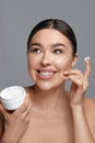 Beautiful smiling woman with healthy smooth facial clean skin applying cosmetic cream and touch own face. Model with Royalty Free Stock Photo