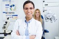 Beautiful smiling woman looking at camera in ophthalmology clinic with woman patient sitting for eye test in background. Royalty Free Stock Photo