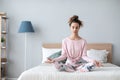 Beautiful smiling woman in lotus pose on bed practicing yoga at home Royalty Free Stock Photo