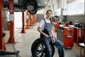 Beautiful smiling woman mechanic sitting on wheel at tire replacement service Royalty Free Stock Photo