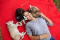 A beautiful smiling woman with a ponytail and wearing a striped shirt is cuddling with three sweet husky puppies while