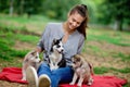 A beautiful smiling woman with a ponytail and wearing a striped shirt is holding three sweet husky puppies while sitting Royalty Free Stock Photo