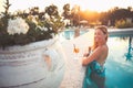 Beautiful smiling woman in the pool with cocktail. Warm lights and intense evening sun Royalty Free Stock Photo