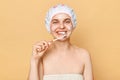 Beautiful smiling woman with tooth brush in hands isolated over beige background brushing her teeth after morning taking shower