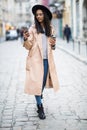 Beautiful smiling woman walking on city street from work with coffee cup and texting on mobile phone Royalty Free Stock Photo