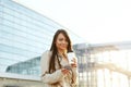 Beautiful smiling woman walking on near office from work with coffee cup and texting on mobile phone.Phone communication. Royalty Free Stock Photo