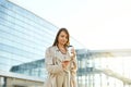 Beautiful smiling woman walking on near office from work with coffee cup and texting on mobile phone.Phone communication. Royalty Free Stock Photo