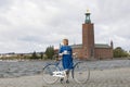 Beautiful smiling woman wearing old fashioned blue dress holding a retro bicycle in front of Stockholm City Hall Royalty Free Stock Photo