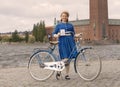Beautiful smiling woman wearing old fashioned blue dress holding a retro bicycle in front of Stockholm City Hall Royalty Free Stock Photo