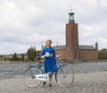 Beautiful smiling woman wearing old fashioned blue dress holding a retro bicycle in front of Stockholm City Hall Royalty Free Stock Photo