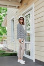 Beautiful smiling woman wearing striped shirt panama and sunglasses standing on porch in front on house in summertime Royalty Free Stock Photo