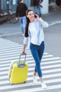 Beautiful smiling woman with yellow travel bag crossing pedestrian and talking