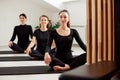 Beautiful smiling women are doing Pilates in a bright studio. Three female athletes in black tracksuits sitting cross