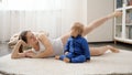 Beautiful smiling woman lying on carpet with baby son and doing fitness exercises. Family healthcare, active lifestyle, parenting Royalty Free Stock Photo