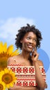 Beautiful, smiling, young african girl wearing clothes with Ukrainian ornament over blue background with sunflowers Royalty Free Stock Photo